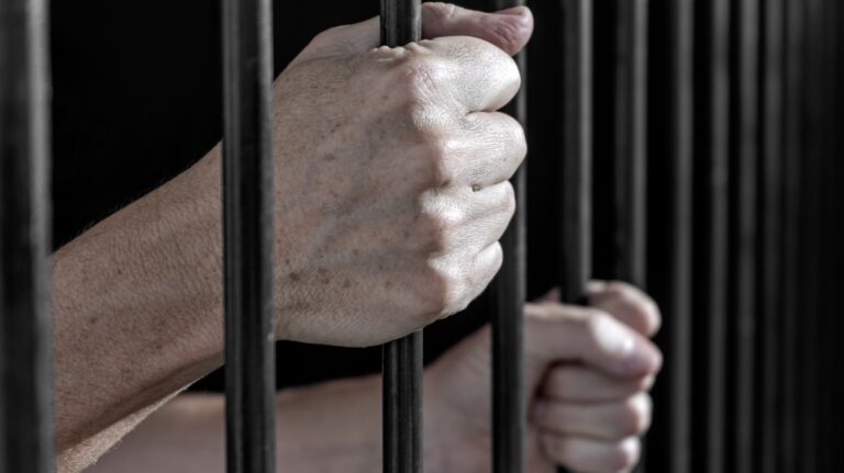 Prisoner's hands gripping the bars of a cell in jail