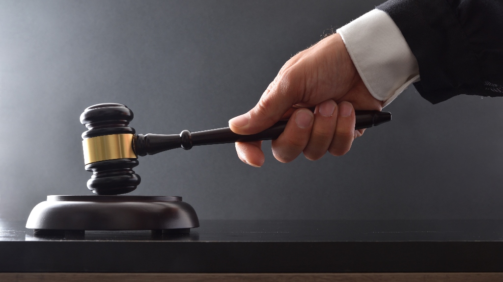 Hand striking on wooden base with judge's gavel on black table