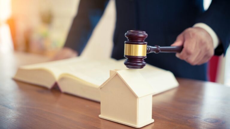 Man's hand holding judge gavel and house model on the desk